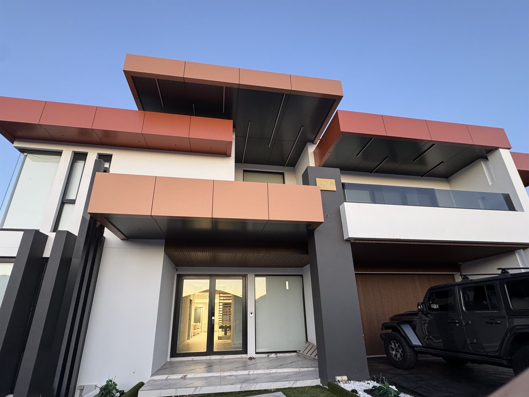 The front of a modern finished Sydney home with terracotta accent panels and a double-height glazed entry