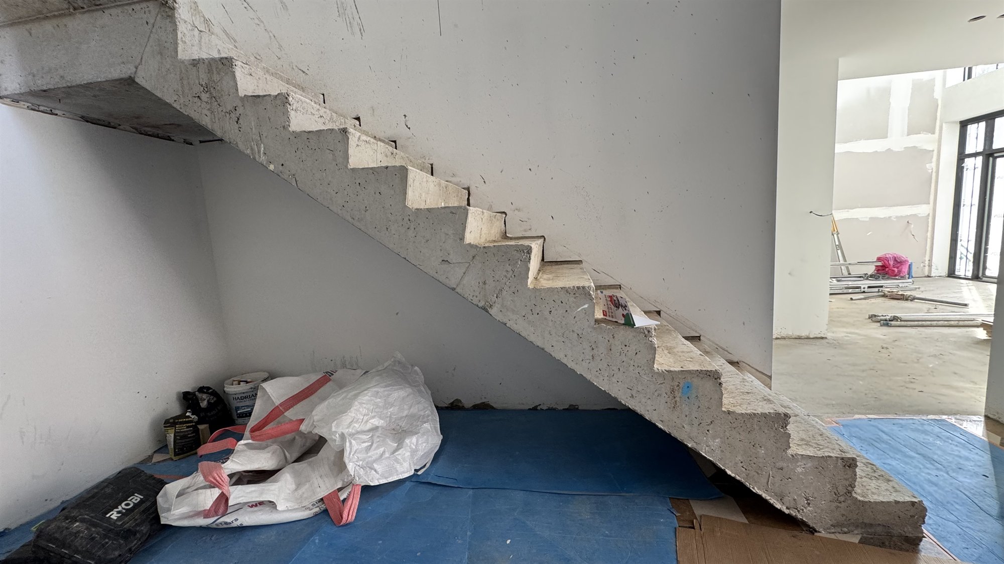 A raw concrete straight staircase under construction in a large Sydney home, beside a double-height room with scaffolding