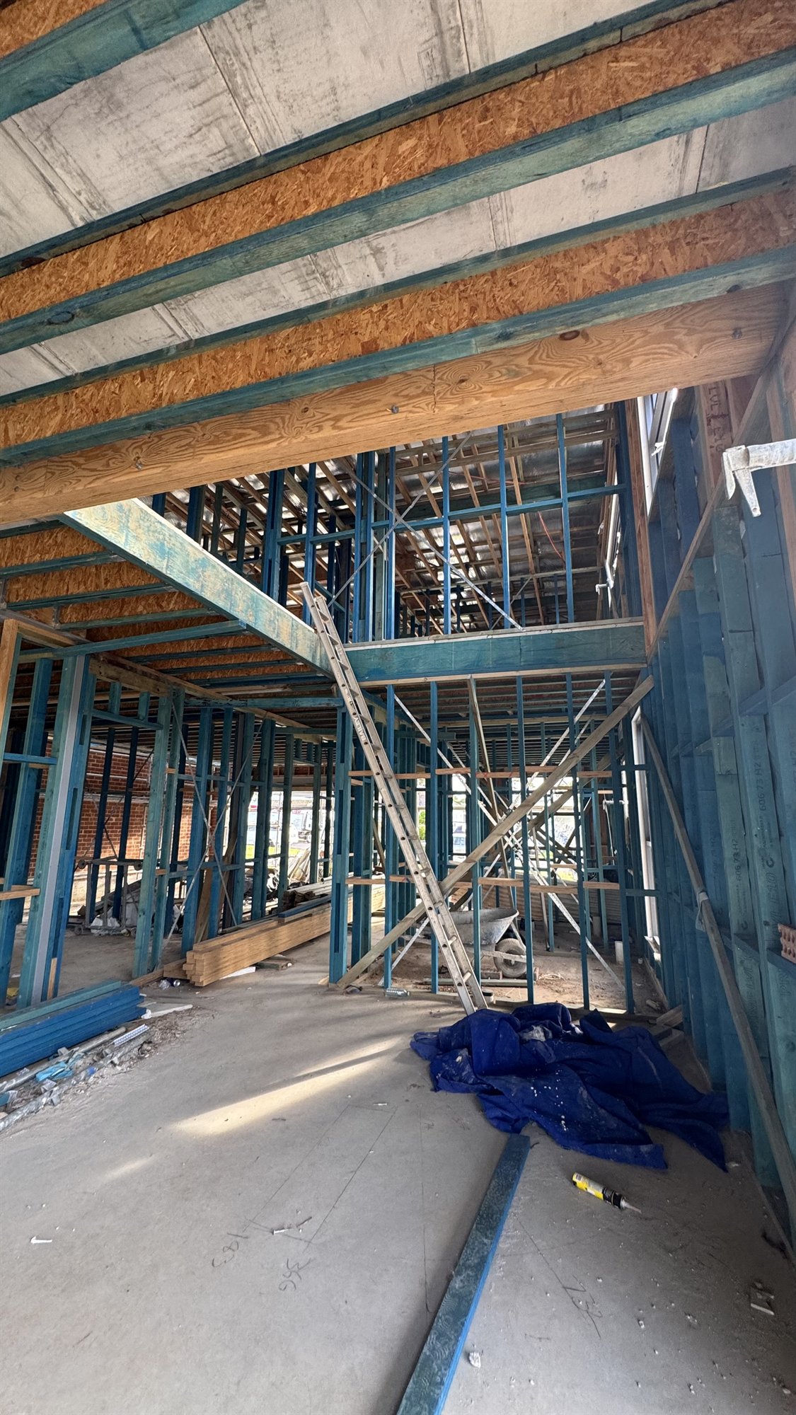 A double-height stair void in a Sydney home under construction, framed in blue steel with timber joists overhead and scaffolding inside