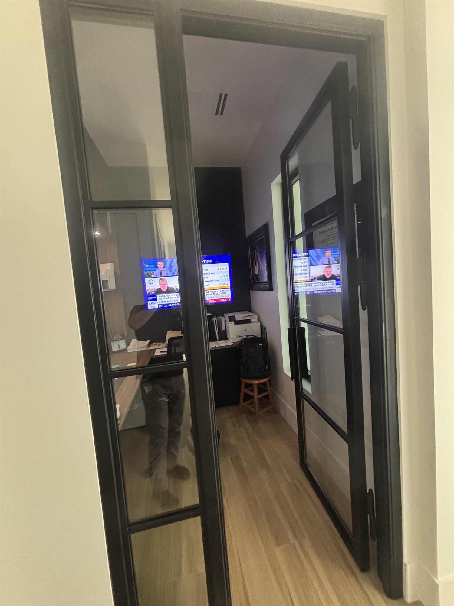A black-framed glass partition with steel-grid doors closing off a home office in a Fort Lauderdale house, light passing through the glass