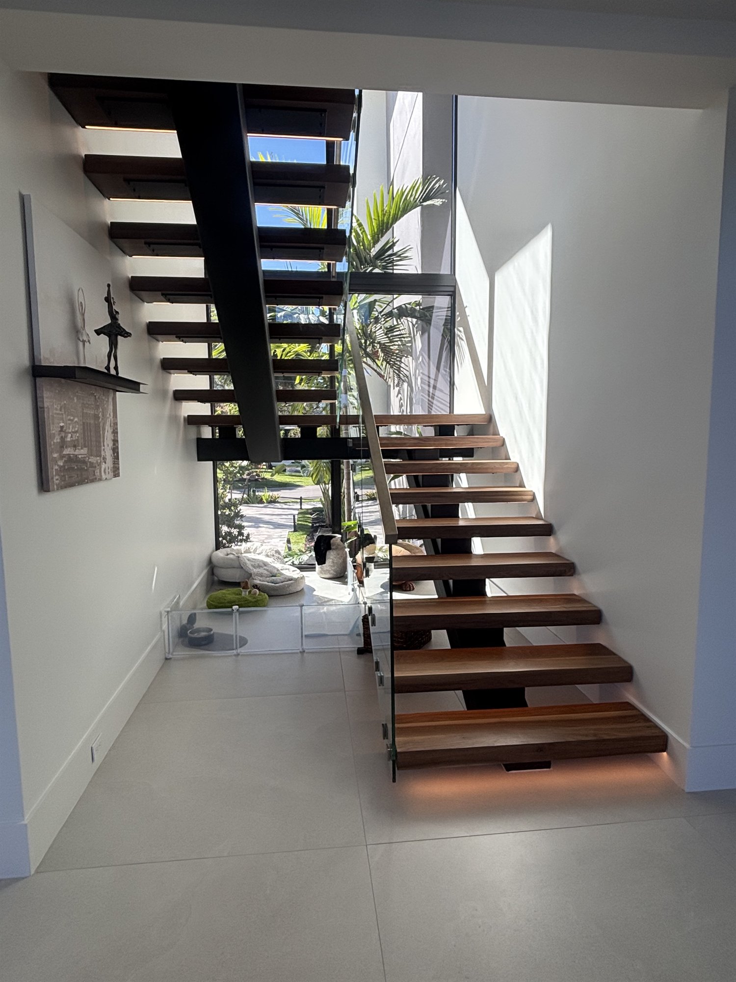 A floating walnut staircase on a black steel mono-stringer with open risers, a frameless glass balustrade and under-tread lighting in a Fort Lauderdale home