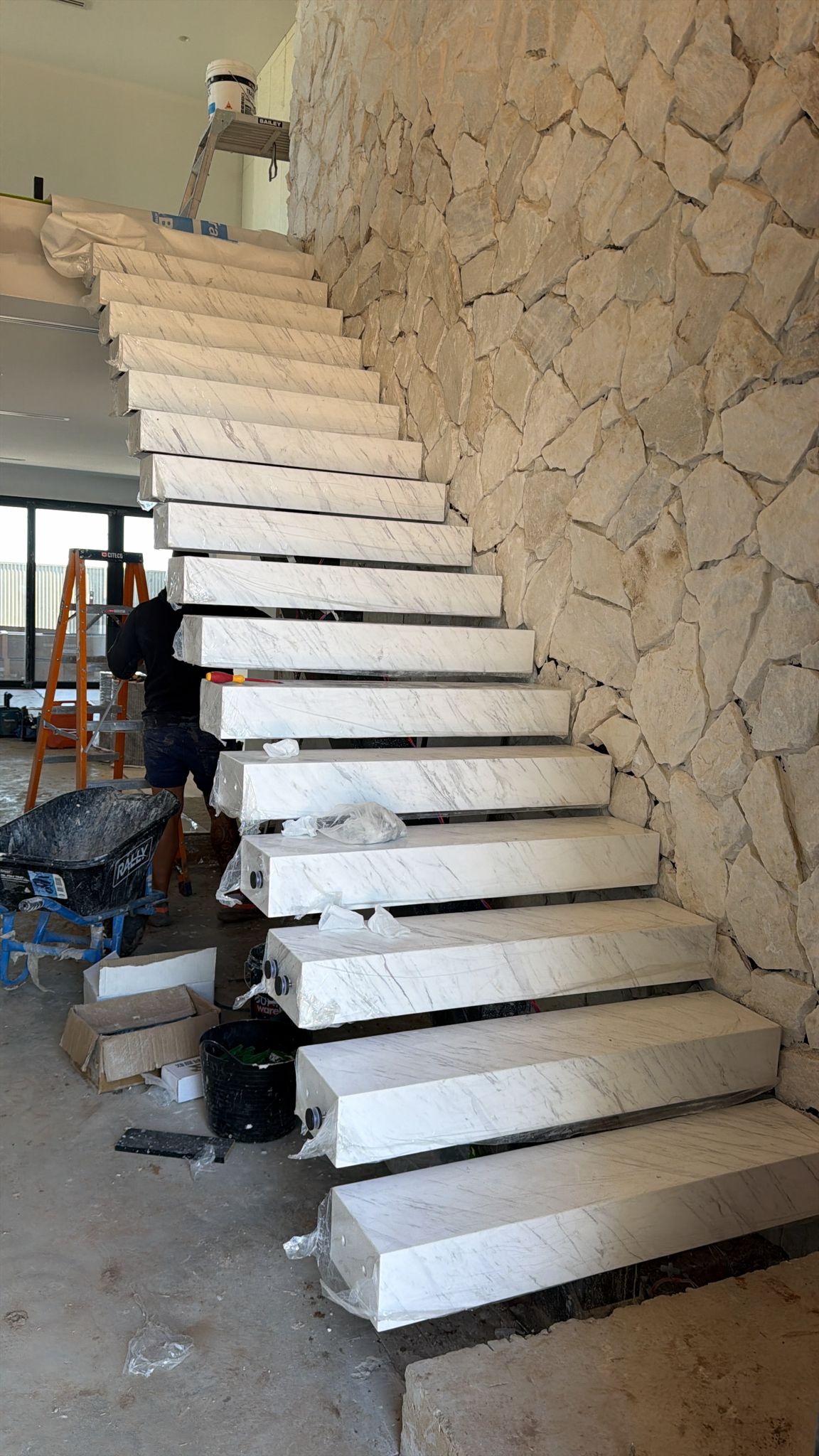 Marble floating staircase treads cantilevering off a natural stone feature wall during fit-out of a new-build home in Adelaide, Australia