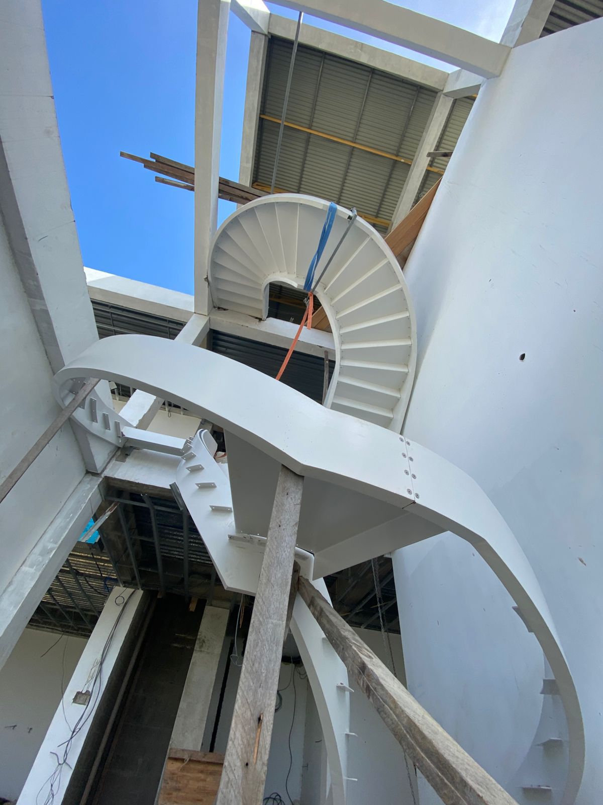 White-painted steel helical staircase structure with curved stringers and bolted flange joints, viewed from below on site in Suriname