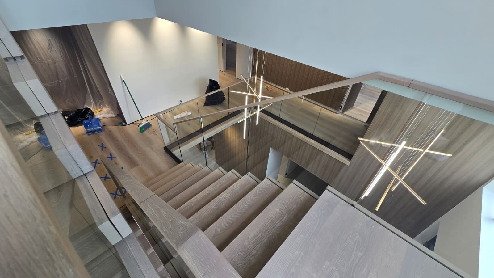 Linear pendant light dropping through the double-height stair void beside the white-oak floating staircase, Florida home