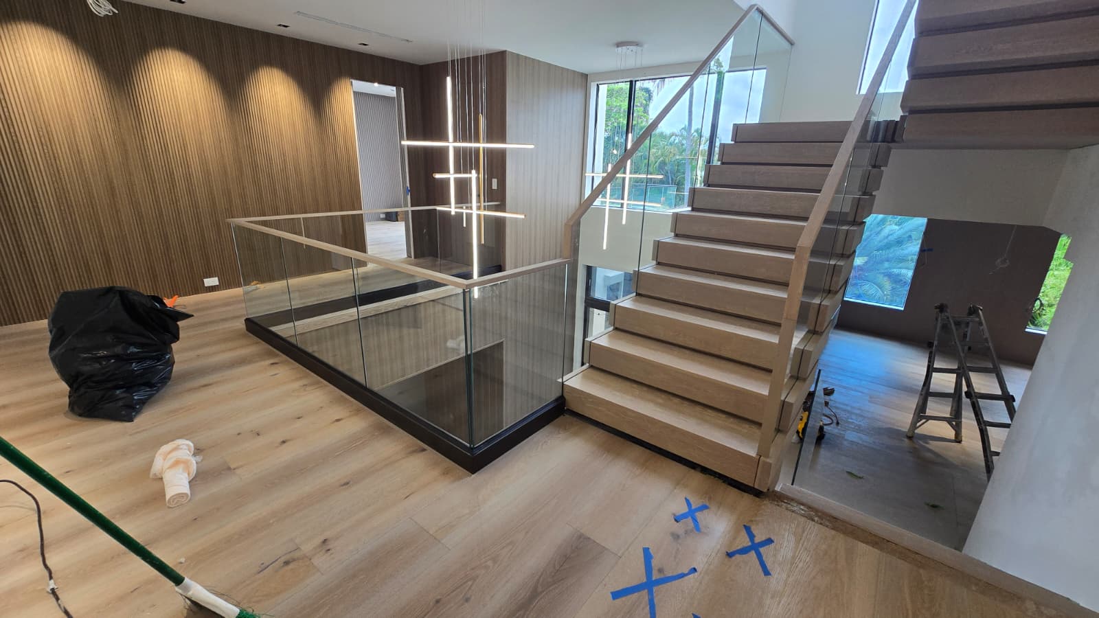 Vertical white-oak slat feature wall beside the floating staircase and frameless glass landing rail in a Florida home