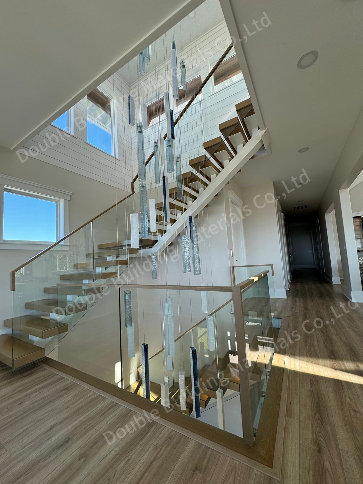 Square-tube floating staircase turning through a vaulted void with oak treads, frameless glass railing and a cascade of pendant lights in a Virginia home