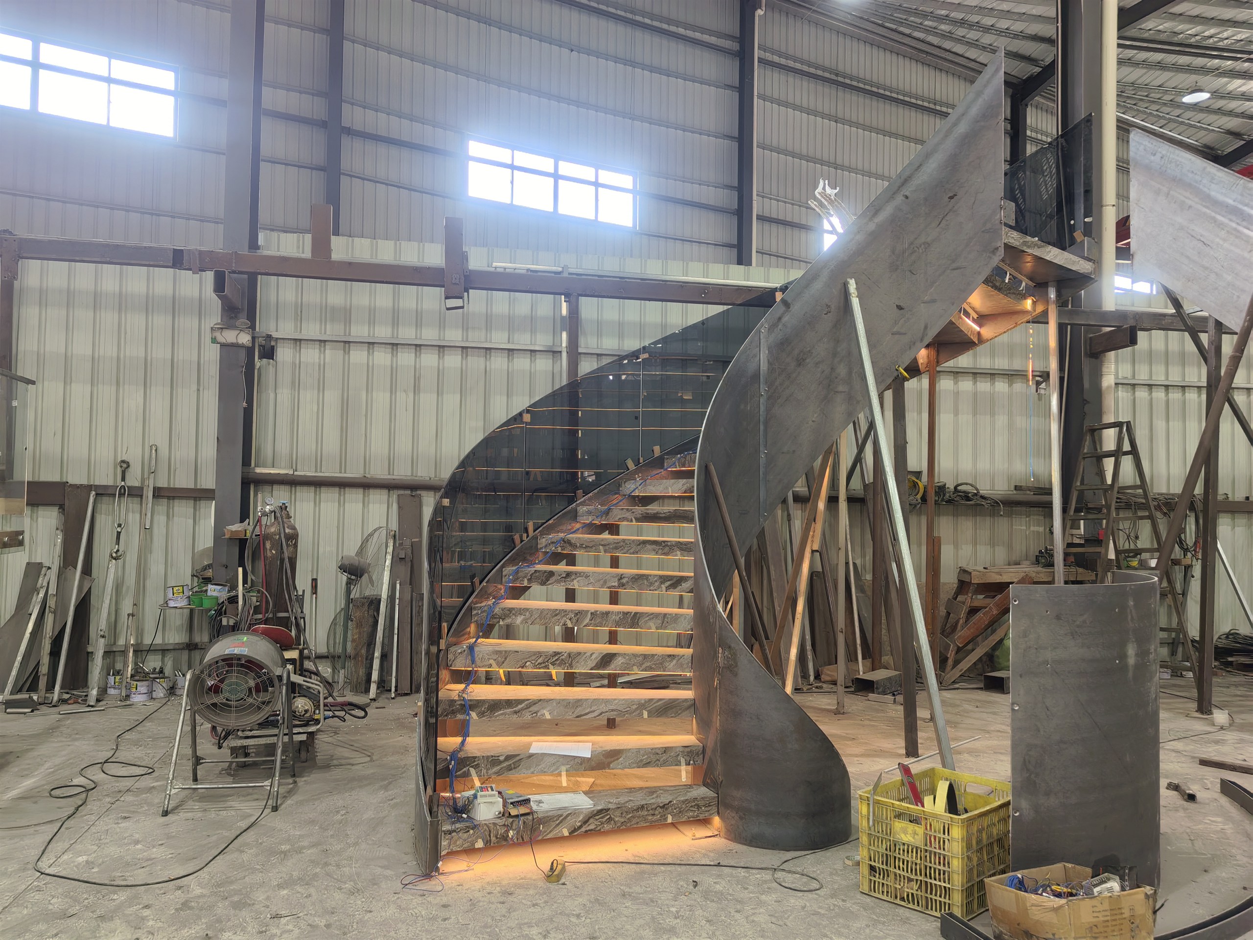 Curved stone staircase with frameless glass railing fully trial-assembled and LED-lit in the DBM Guangdong workshop before shipping