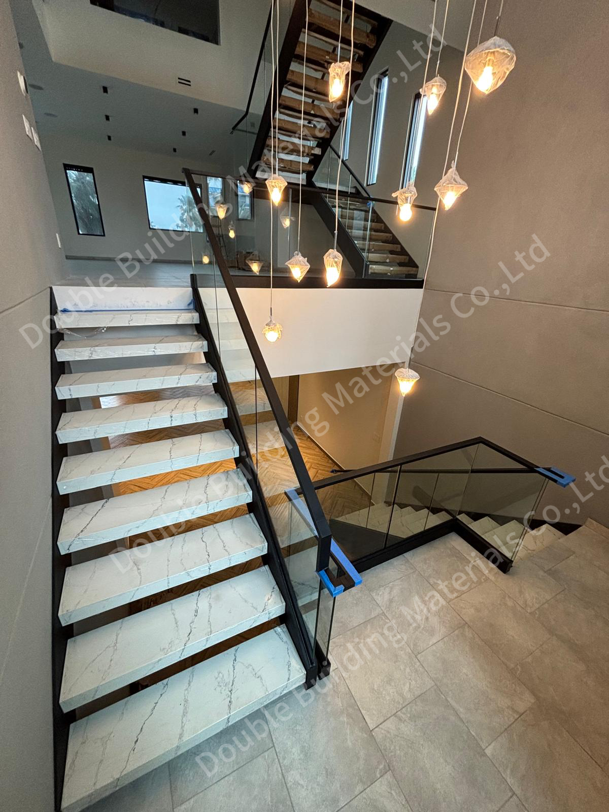Stone staircase with frameless glass railing and a cascade of crystal pendant lights in a tall double-height stair hall, Texas home