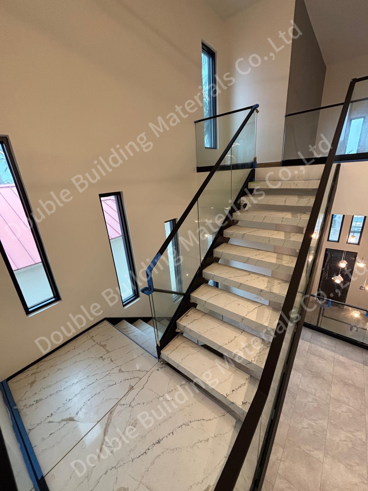Frameless glass railing with a dark top rail beside a stone-tread staircase in a tall double-height stair hall, Texas home