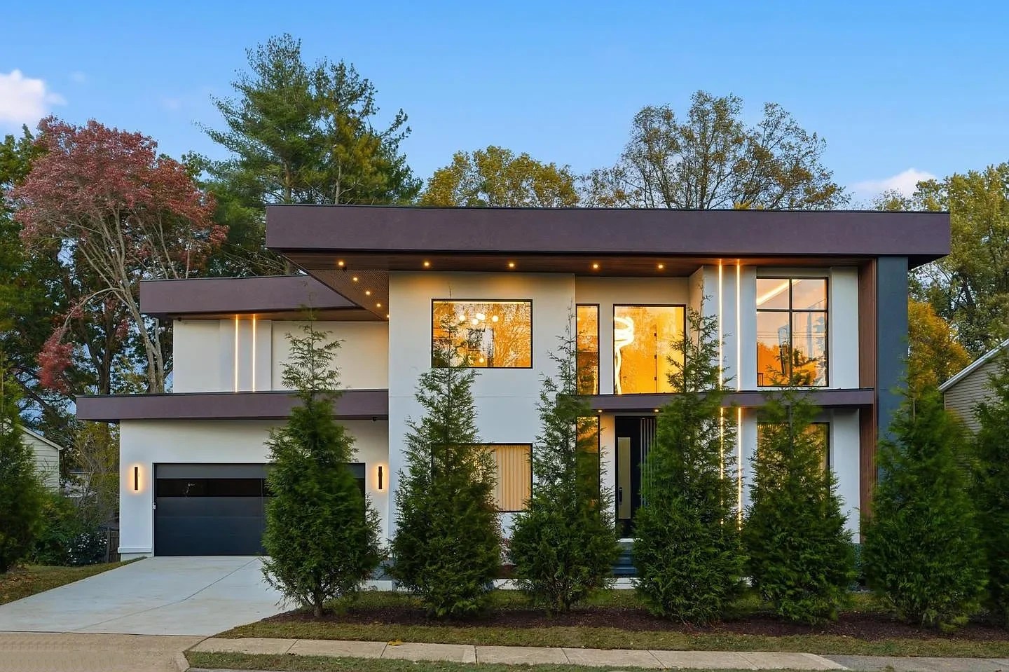 Front of a modern two-storey home in Virginia at dusk with a dark garage door, white walls and black-framed windows