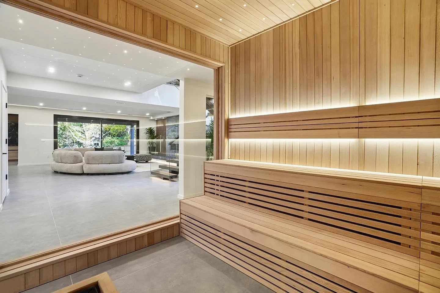 View from inside a timber sauna through its full glass front to the lower-level lounge and stair of a Virginia home
