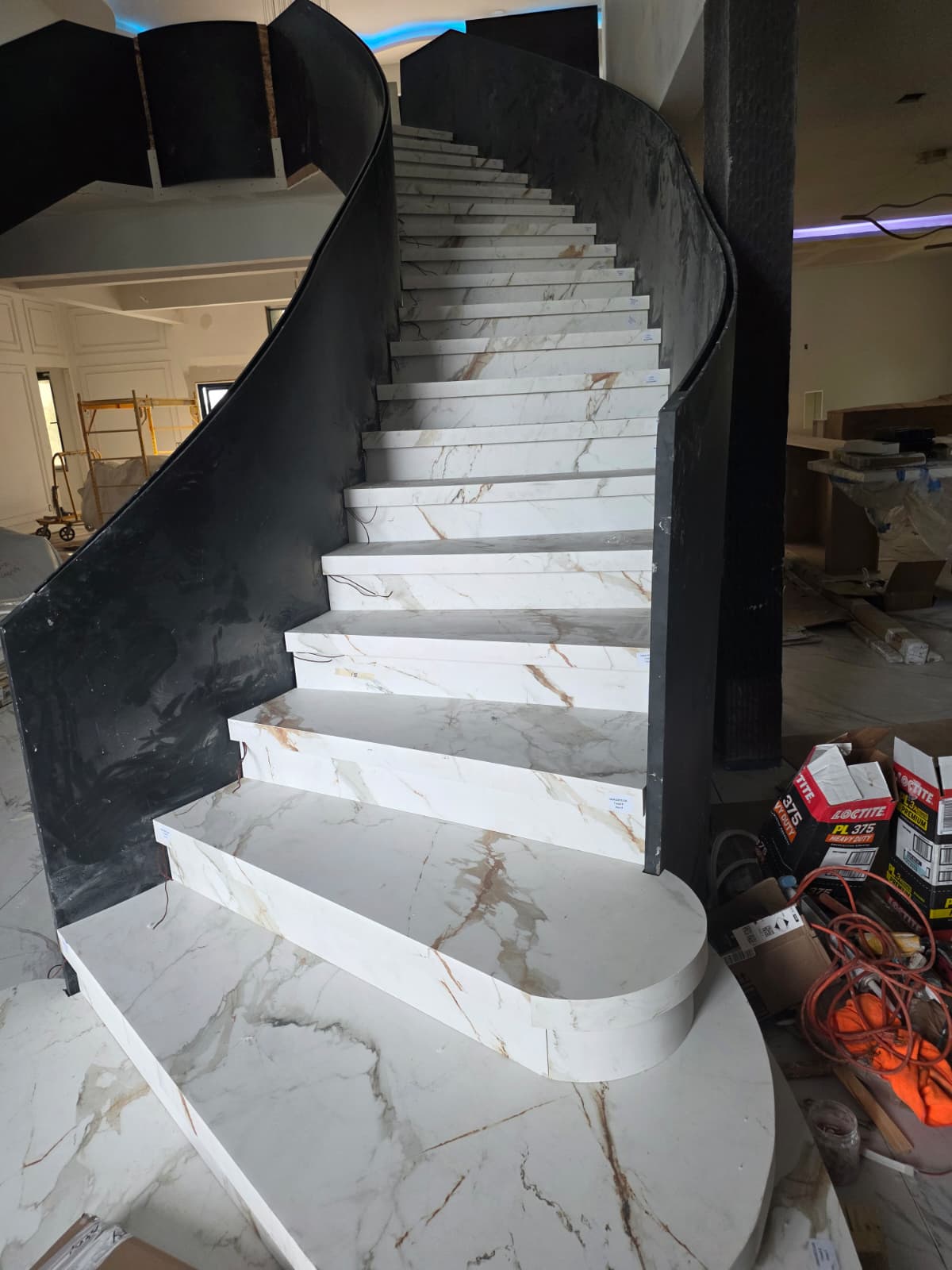 Double curved staircase run with white sintered stone treads and closed risers between tall black steel plate stringers, New Albany, Ohio