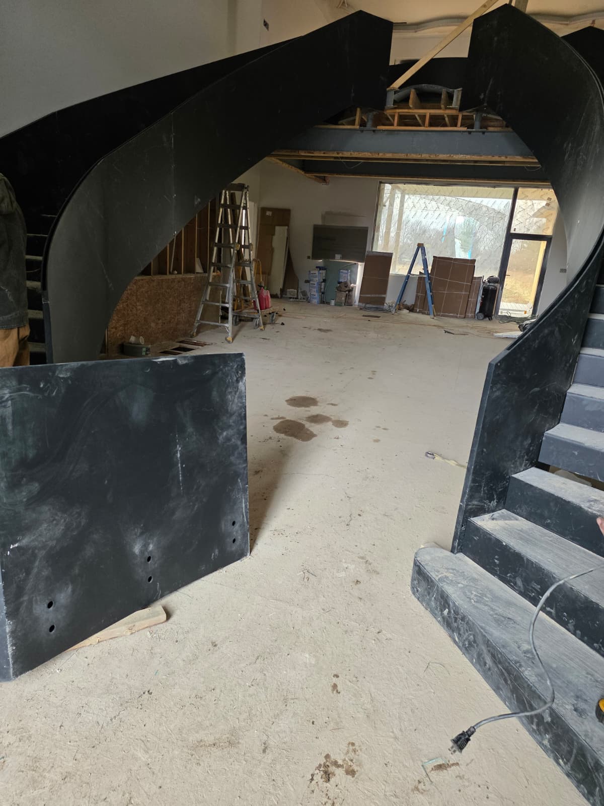 Two curved steel plate staircase runs rising toward each other in an unfinished hall, one run still showing bare steel steps, Ohio