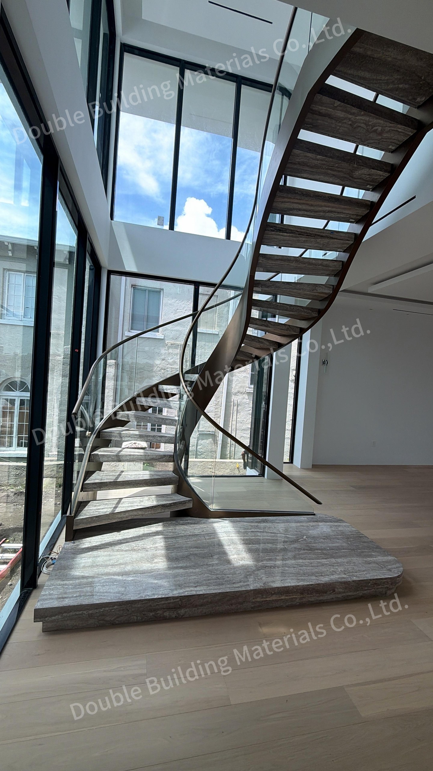 Curved staircase with travertine treads, open risers, brass-tone stringers and a curved glass balustrade in a glass-walled room, Miami