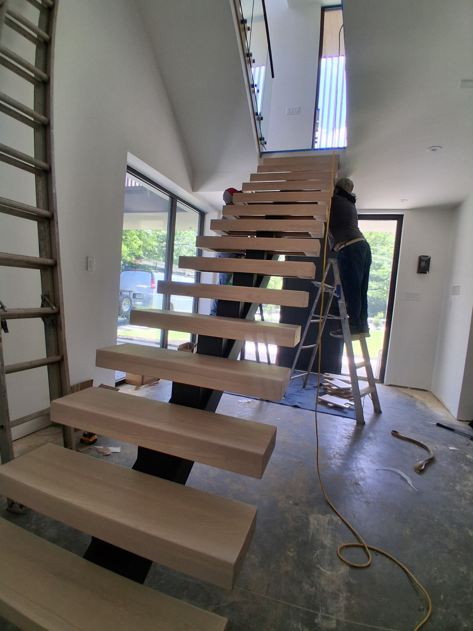 Square-tube mono-stringer staircase with solid ash treads during fitting in an Atlanta home, standoff glass railing above