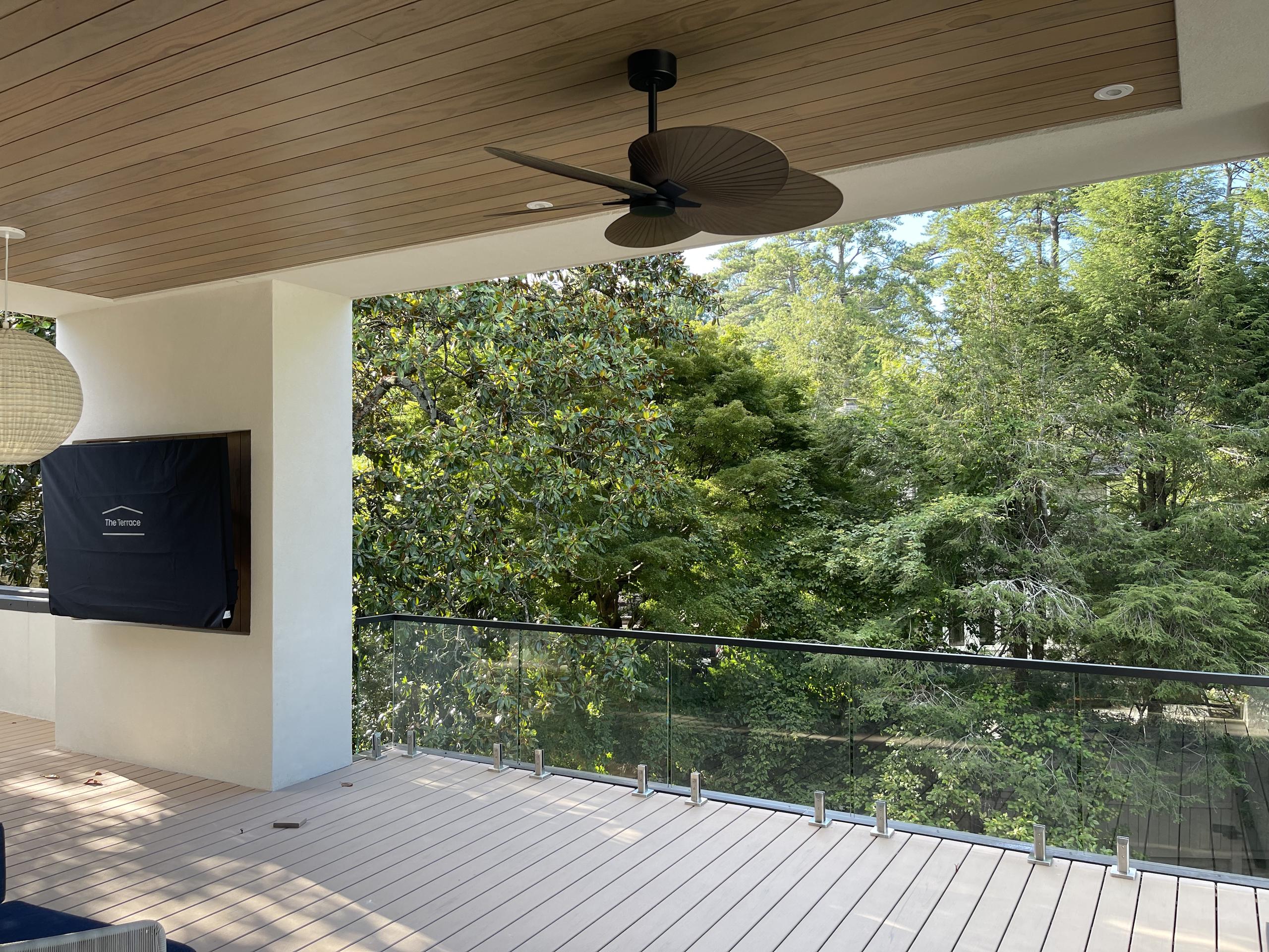 Covered deck with spigot glass railing, bright metal spigots and a black top rail in front of tall trees in Atlanta