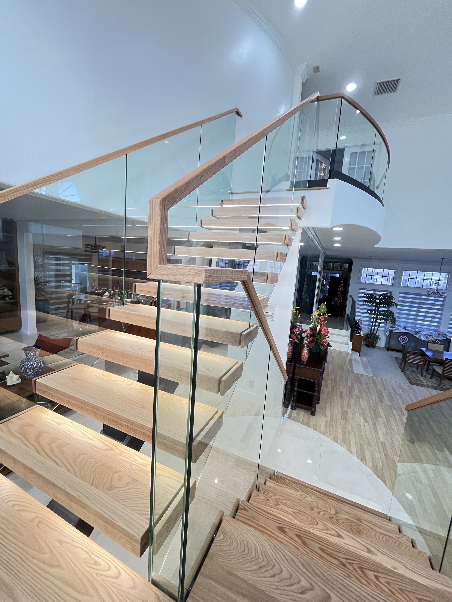 Red oak upper flight with glass and a wood handrail rising to a curved glass railing at the upper landing of a Hawaii home