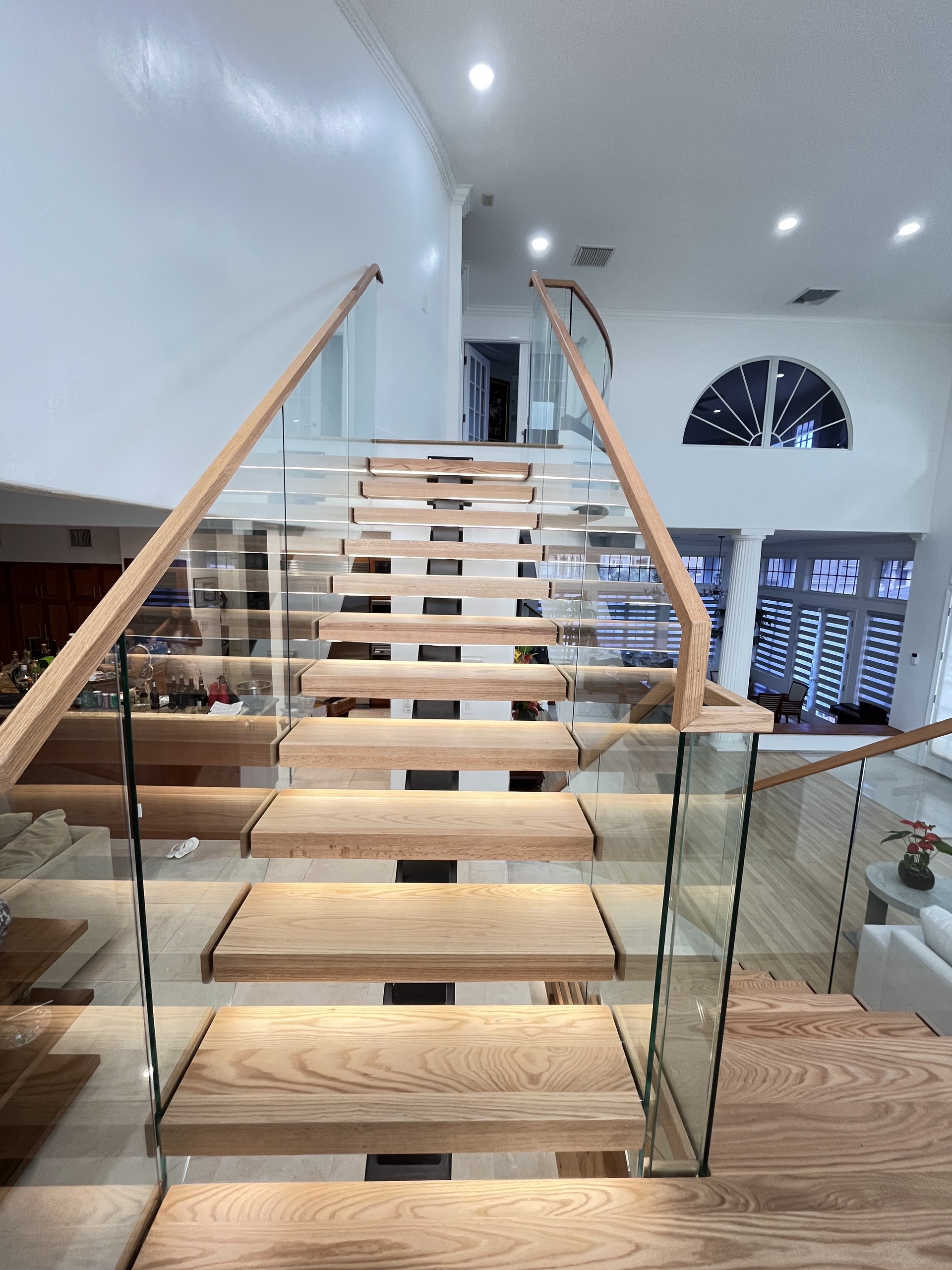 Looking up the red oak upper flight from the landing, with glass on both sides, a wood handrail and LED light under each tread