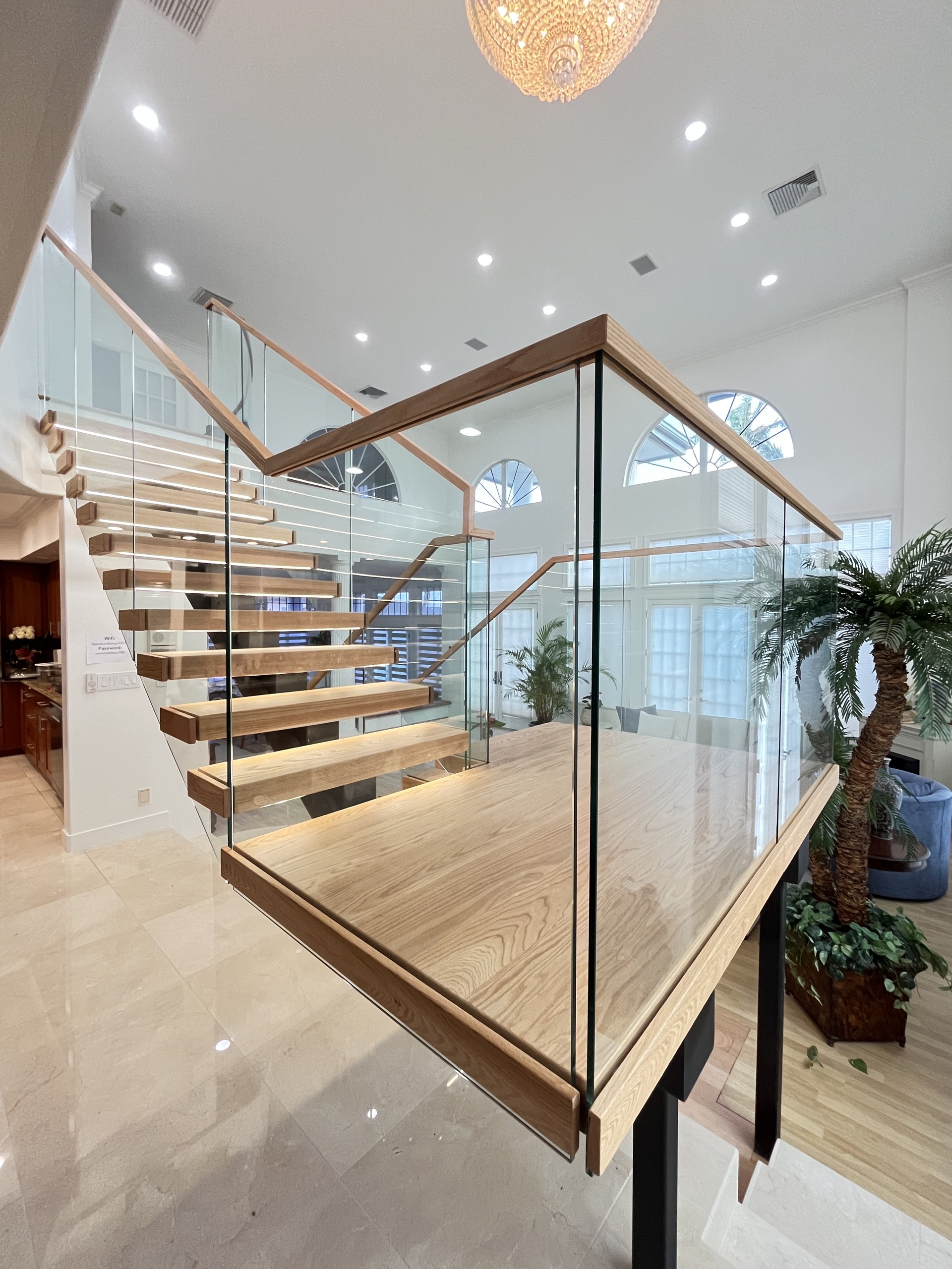 Corner of the red oak landing with glass panels and a wood handrail, the lower treads lit from below, in a Hawaii home