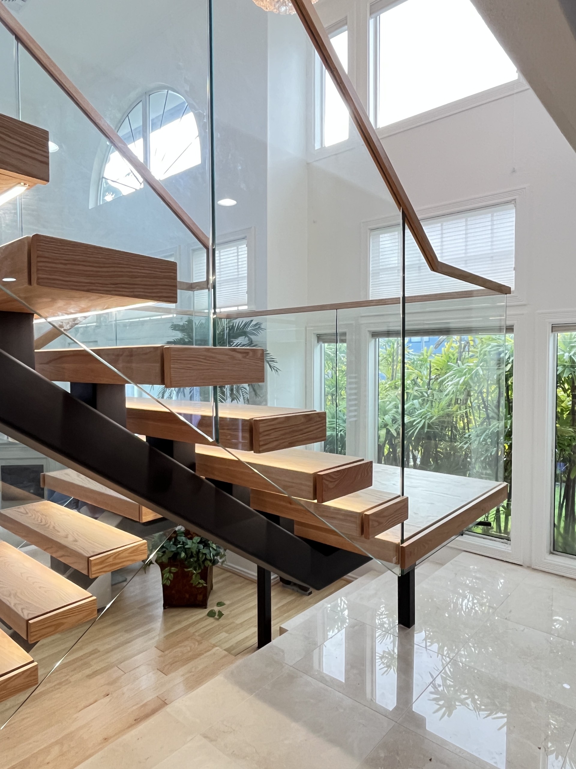 Black square-tube stringer under red oak treads with short steel blocks, frameless glass and a black post under the landing