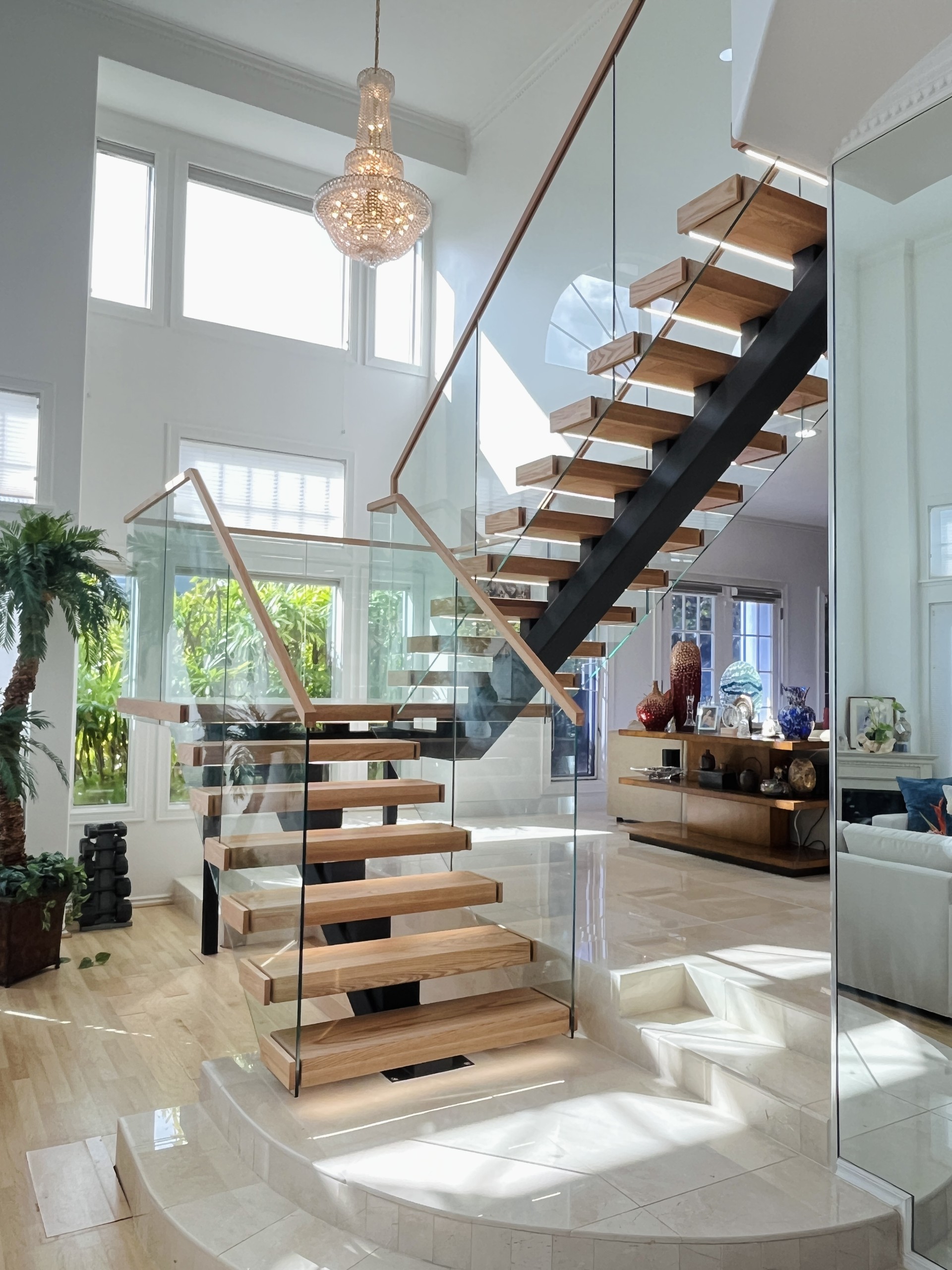 U-shaped staircase with red oak treads on a black square-tube stringer and frameless glass with a wood handrail, in a tall Hawaii living room